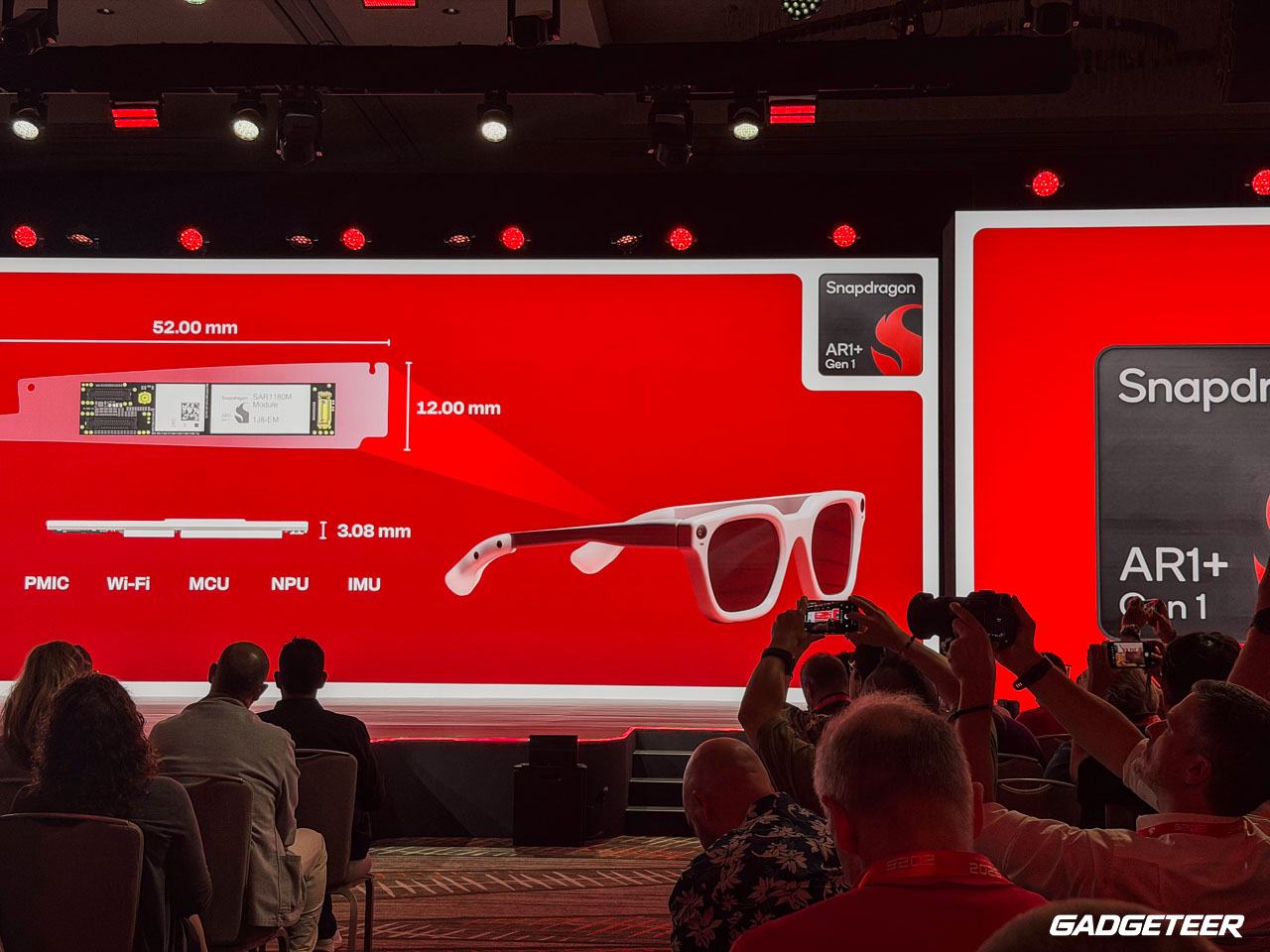 Photograph of the Snapdragon Summit stage showing white smart glasses, a compact hardware module, and the Snapdragon AR1+ Gen 1 logo.